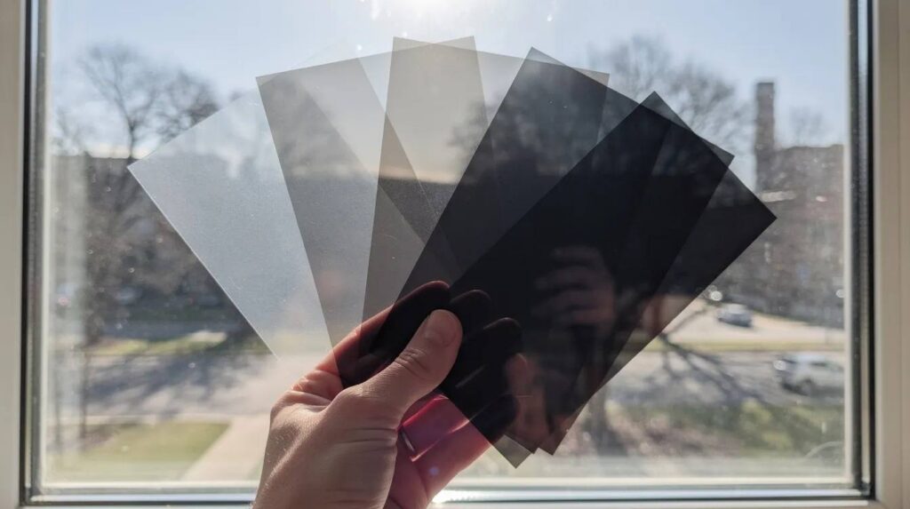 The image displays several samples of uv window film held against sunlit glass, showcasing various levels of tint and clarity. These films are designed to protect against harmful uv rays, reduce sun damage, and enhance the comfort of indoor spaces by controlling glare and heat.